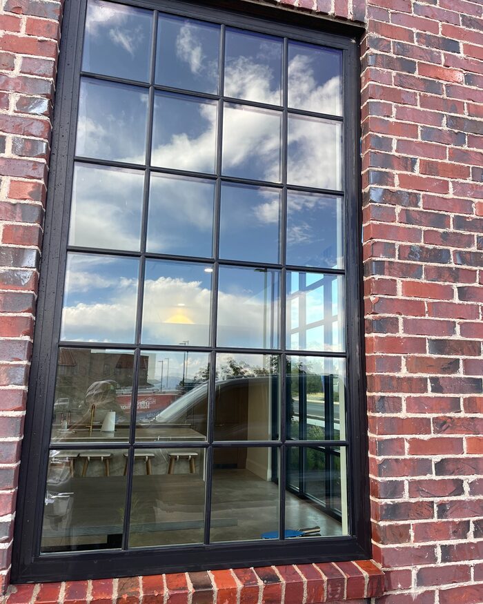 A clean exterior window in a brick wall reflecting blue sky and clouds.