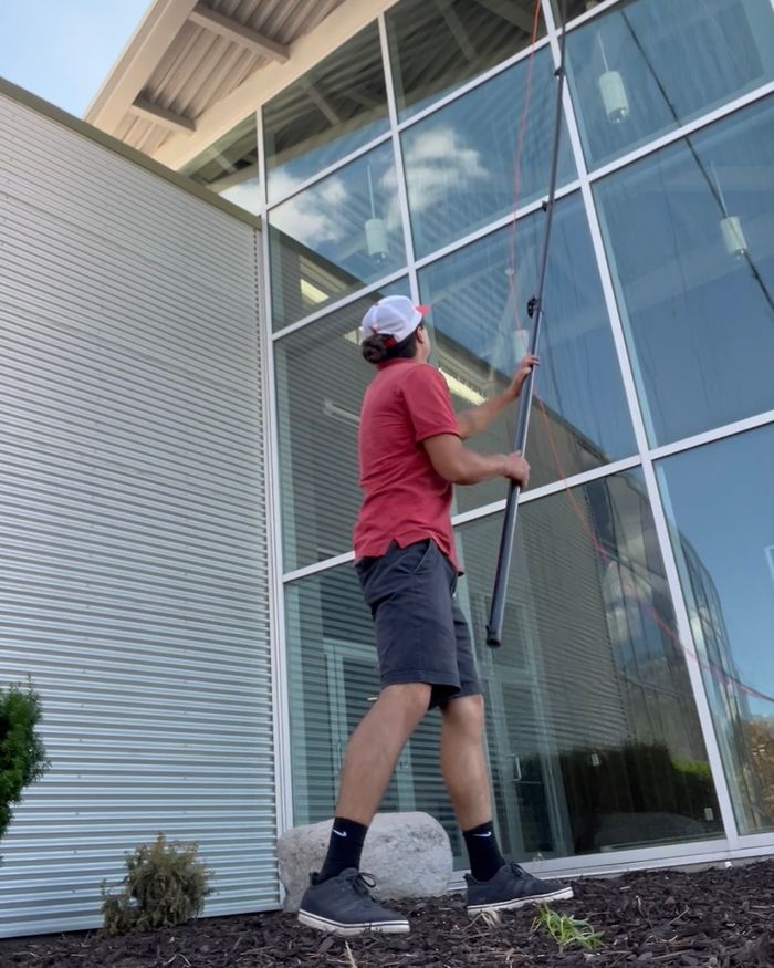 A NestWise technician using a water-fed pole to clean a two-story wall of commercial glass.