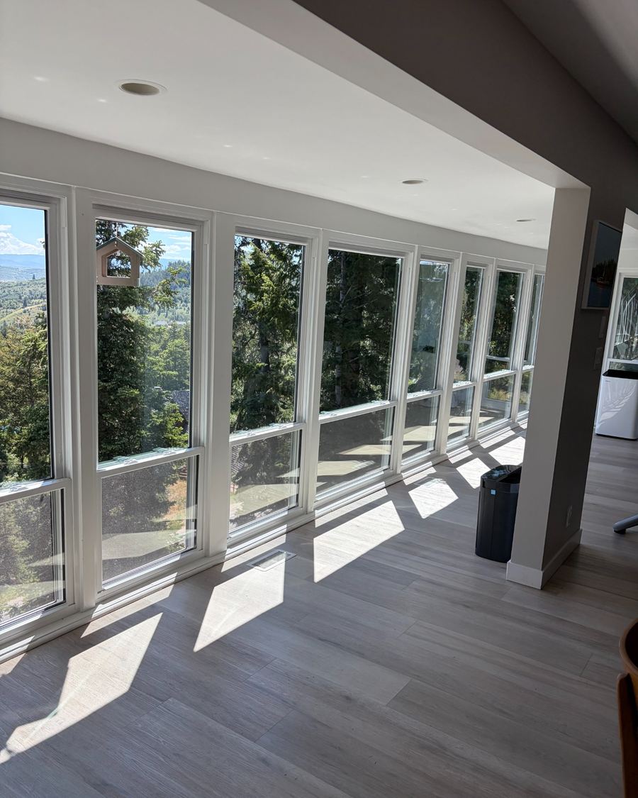 A bright living room with a wall of tall, clean windows overlooking trees and a hillside.