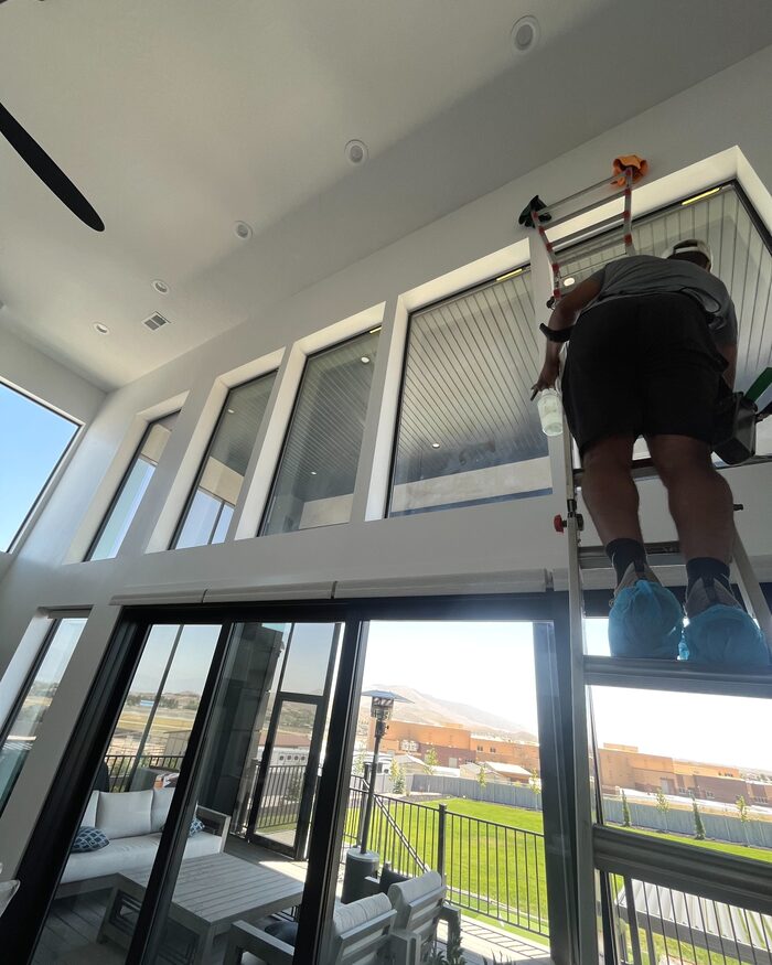 A window cleaner standing on a ladder while cleaning tall interior windows.