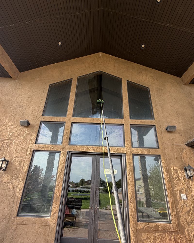 A water-fed pole rinsing the tall entry windows of a stucco home.