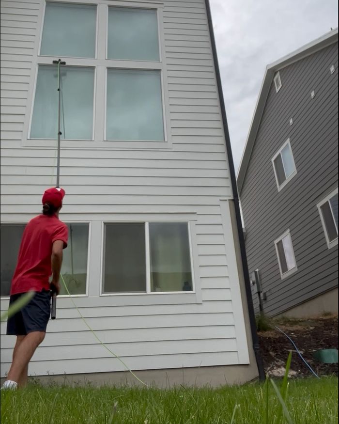 A NestWise technician using a water-fed pole to reach upper-story windows on a home.