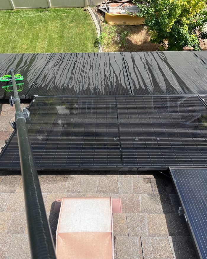 Roof-mounted solar panels being cleaned with a water-fed pole.