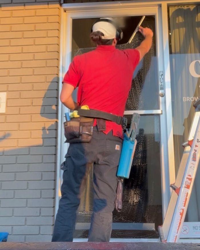A NestWise technician squeegeeing the glass door of a commercial storefront with a ladder set alongside.