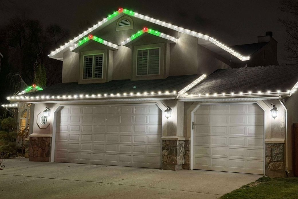 A home outlined along every roofline with warm white traditional Christmas lights, with red and green accents on the gables.